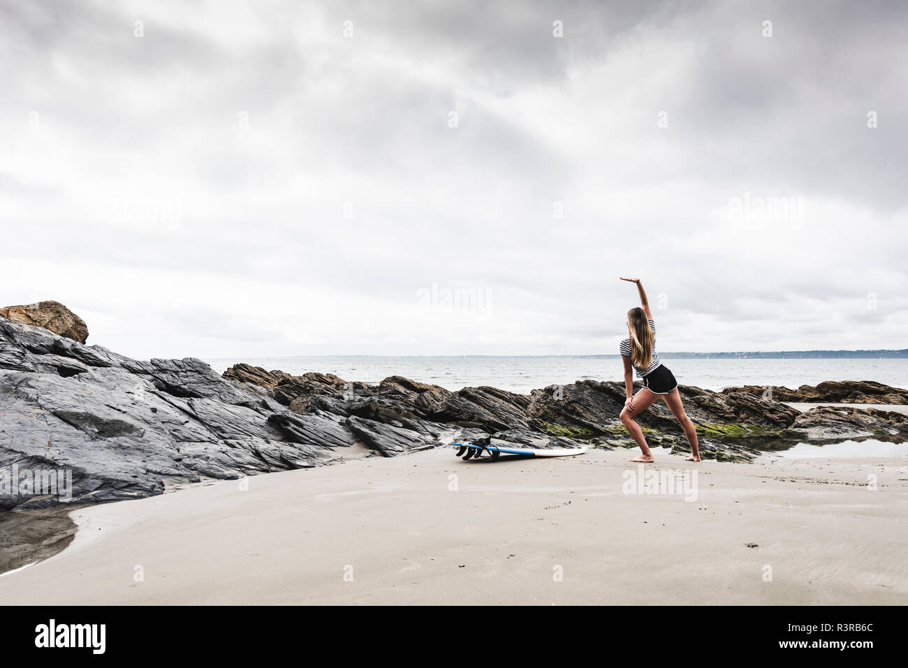 Junge Frau mit Surfbrett stretching am Strand Stockfoto