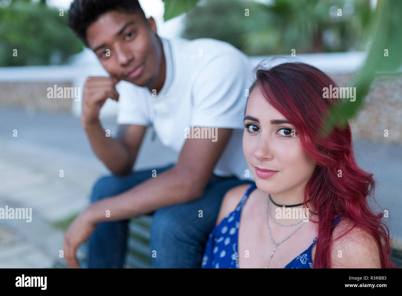 Porträt der jungen Frau mit rot gefärbten Haaren sitzt auf der Bank mit ihrem Freund Stockfoto