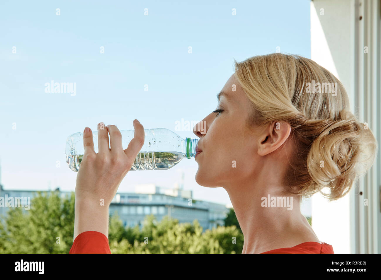 Junge Frau trinkt Wasser aus der Flasche am Fenster Stockfoto