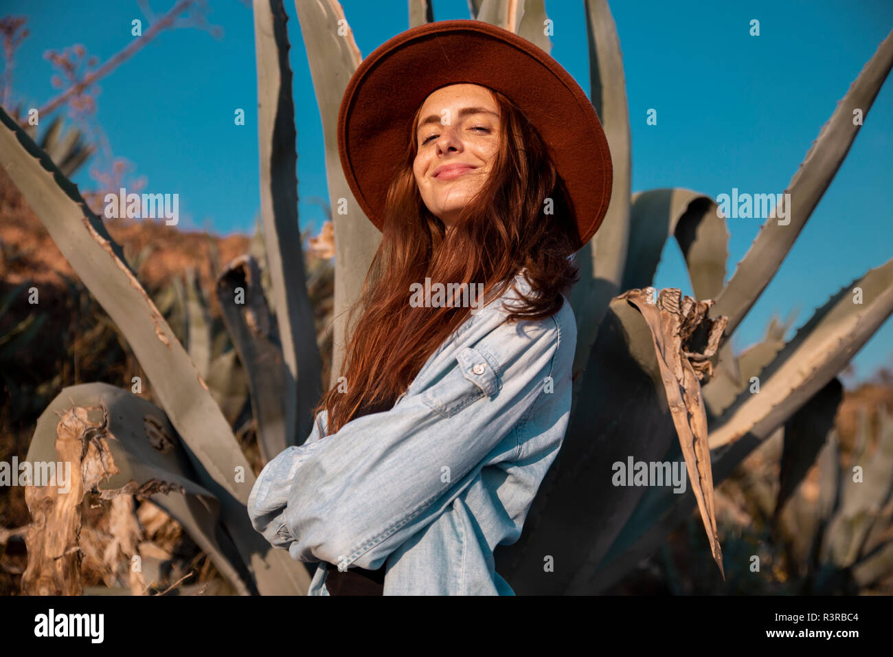 Lächelnde junge Frau mit Hut in einer Agave in ländlicher Welt Stockfoto