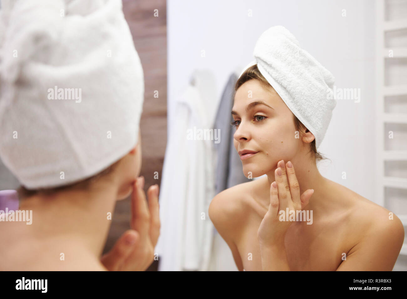 Spiegelbild der jungen Frau ihr Gesicht Prüfung im Badezimmer Stockfoto