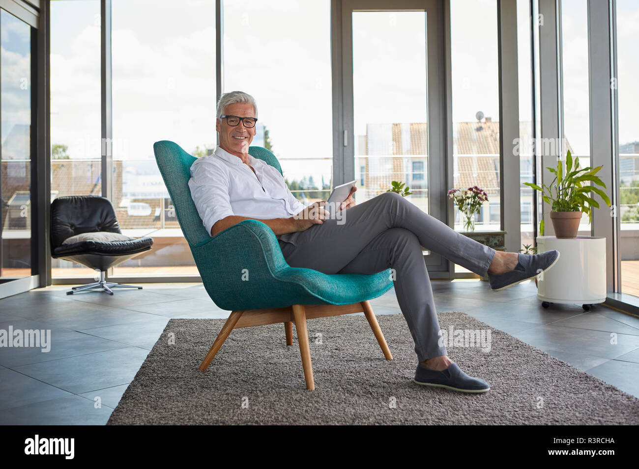 Portrait von reifer Mann im Sessel zu Hause holding Tablet sitzen Stockfoto