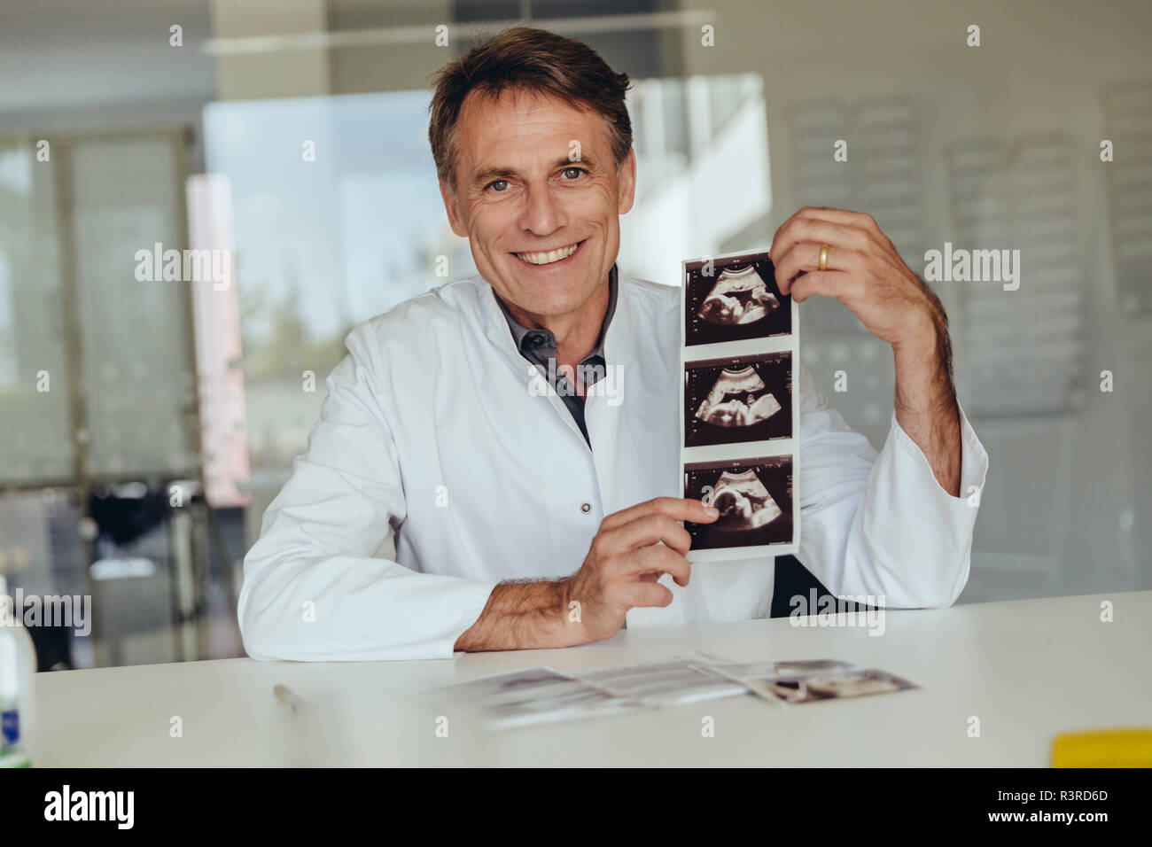 Arzt sitzen am Schreibtisch, mit Ultraschall eines Fötus Scan Stockfoto