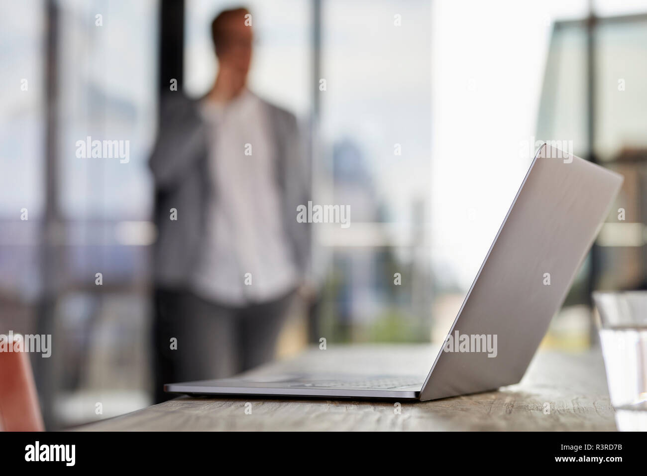 Laptop auf dem Schreibtisch im Büro mit Geschäftsmann im Hintergrund Stockfoto