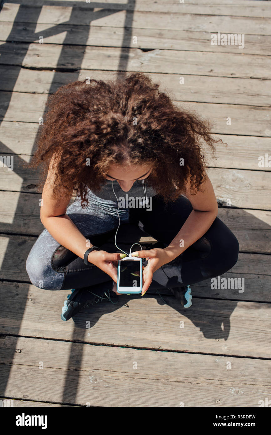Junge athletische Frau sitzt auf der Promenade mit Smartphone Stockfoto