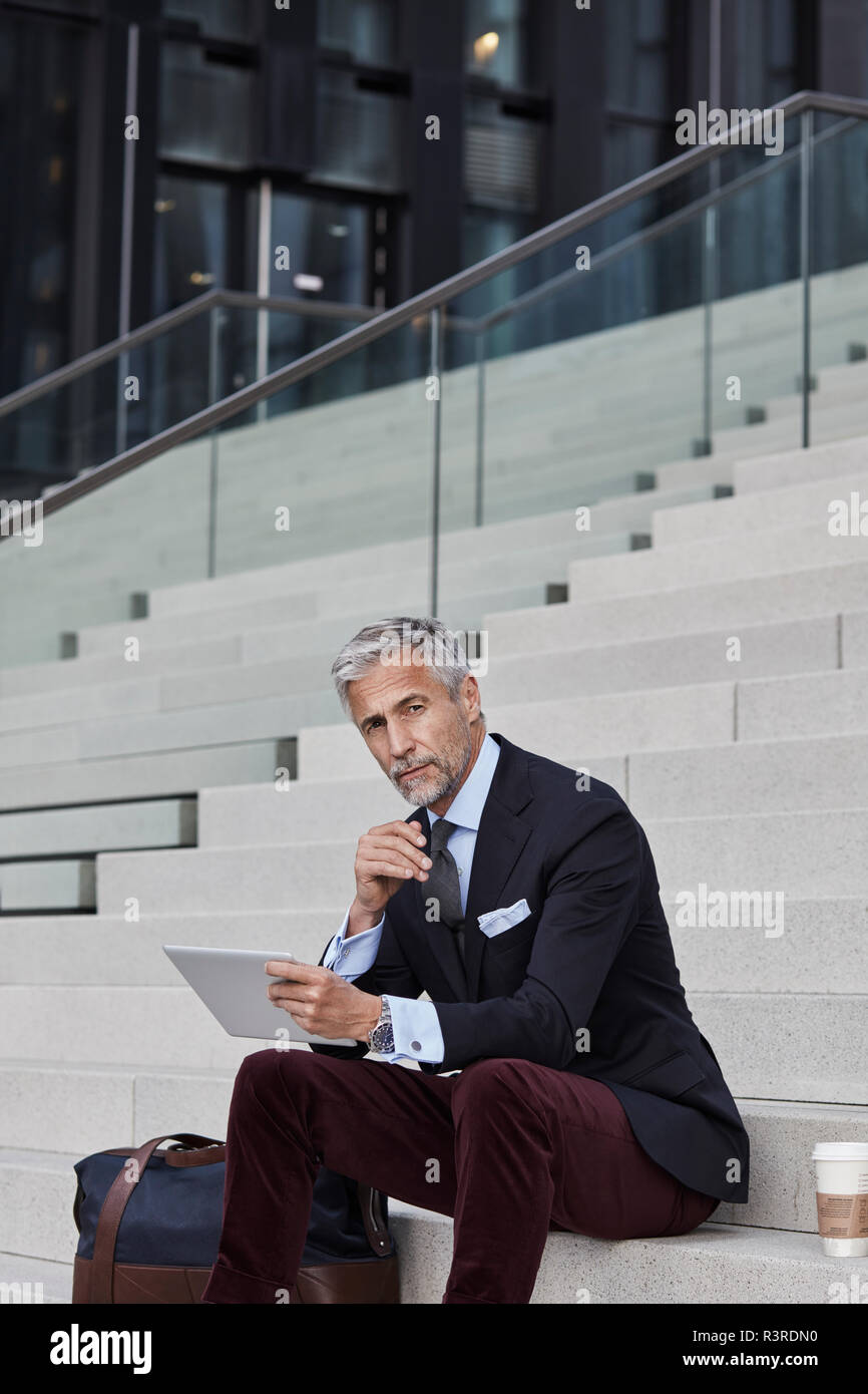 Portrait von modischen Geschäftsmann mit Reisetasche, Kaffee trinken gehen und Tablet sitzen auf Treppen Stockfoto