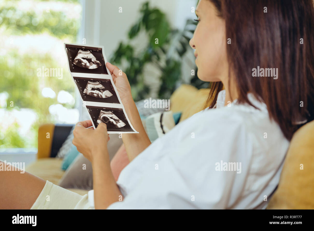 Frau auf der Suche nach Ultraschall Bilder von ungeborenen Kind auf der Couch Stockfoto