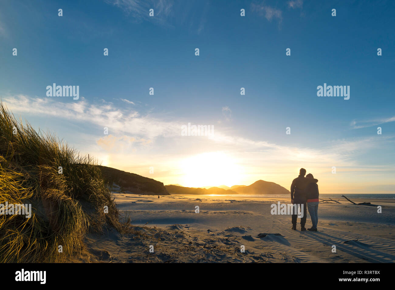 Neuseeland, Südinsel, Puponga, Wharariki Beach, Paar am Strand bei Sonnenuntergang Stockfoto