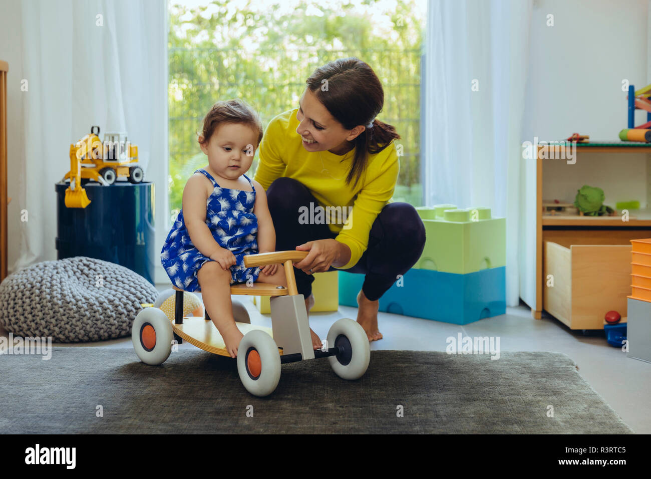 Glückliche Mutter mit Baby auf spielzeugauto im Wohnzimmer Stockfoto