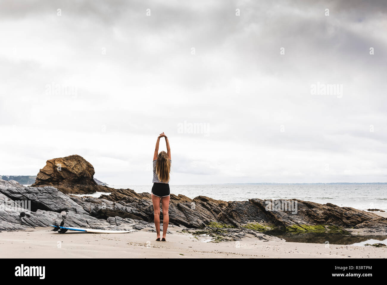 Junge Frau mit Surfbrett stretching am Strand Stockfoto