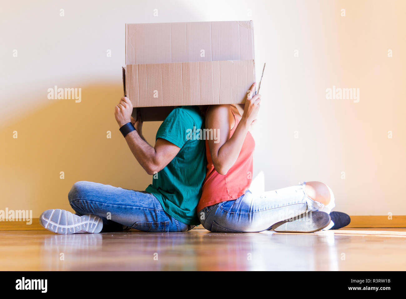 Paar mit Kopf im Karton Rücken an Rücken auf dem Boden sitzend im neuen Zuhause Stockfoto