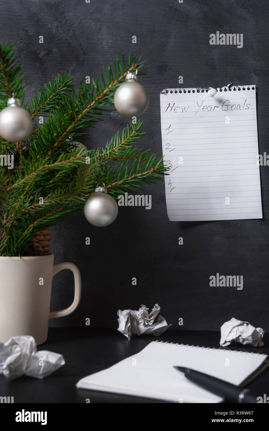 Liste mit Zielen für das neue Jahr auf einem Notebook zu einem Büro Wand, zerknittertes Papier und Kiefer Äste auf den Schreibtisch. Ziele Planung Konzept. Stockfoto
