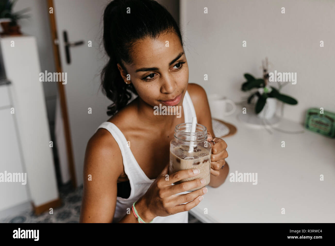 Porträt der jungen Frau mit Glas Eiskaffee in der Küche Stockfoto