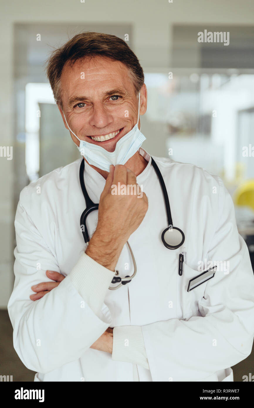 Porträt eines Arztes, Entfernen von Op-Maske, lächelnd Stockfoto