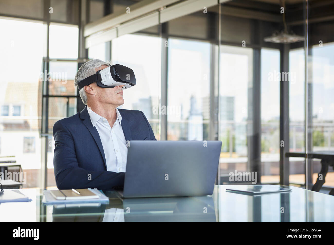 Geschäftsmann am Schreibtisch mit Laptop sitzen, mit VR-Brille Stockfoto