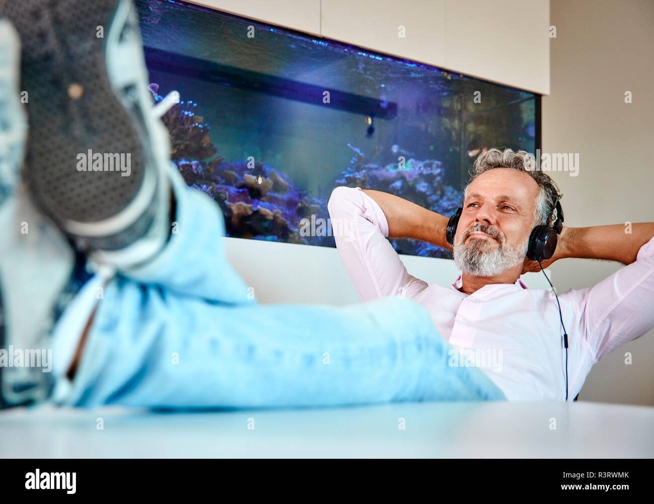 Entspannt reifer Mann Hören von Musik über Kopfhörer vor Aquarium Stockfoto
