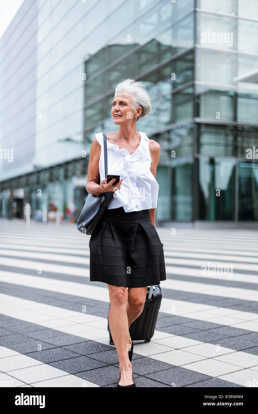 Ältere Frau mit Handy und Gepäck unterwegs Stockfoto