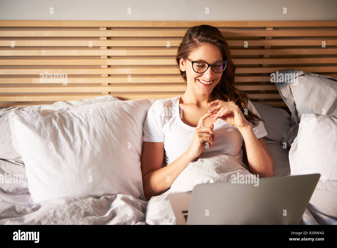 Portrait von lächelnden jungen Frau auf dem Bett liegend mit Laptop Stockfoto