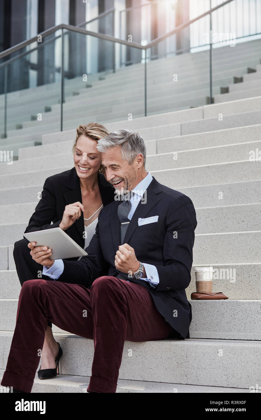 Zwei Geschäftsleute sitzen zusammen auf der Treppe am Tablet suchen Stockfoto