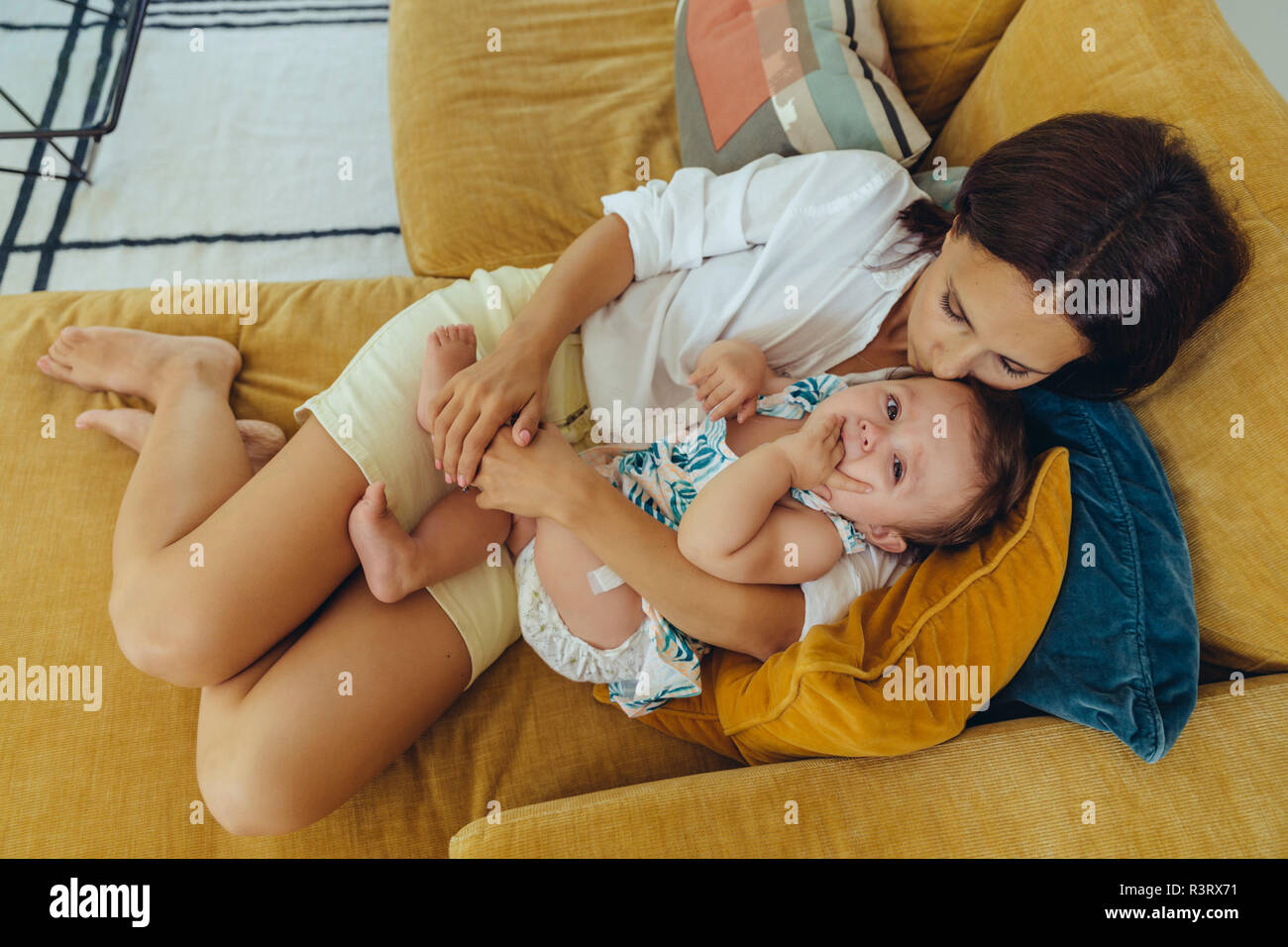 Mutter kuscheln und küssen ihr Baby Mädchen auf der Couch Stockfoto