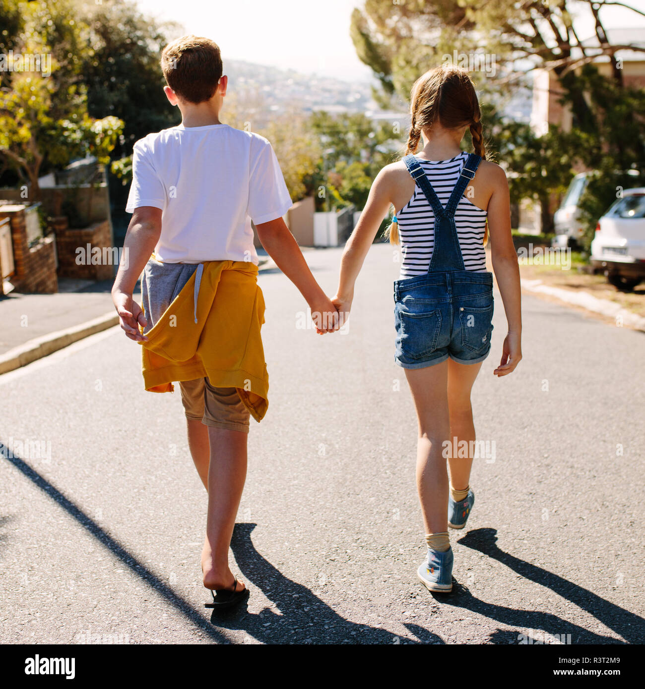 Rückansicht eines Jungen und Mädchen gehen auf eine leere Straße. Kinder gehen zusammen auf der Straße ihre Hände halten an einem sonnigen Tag. Stockfoto