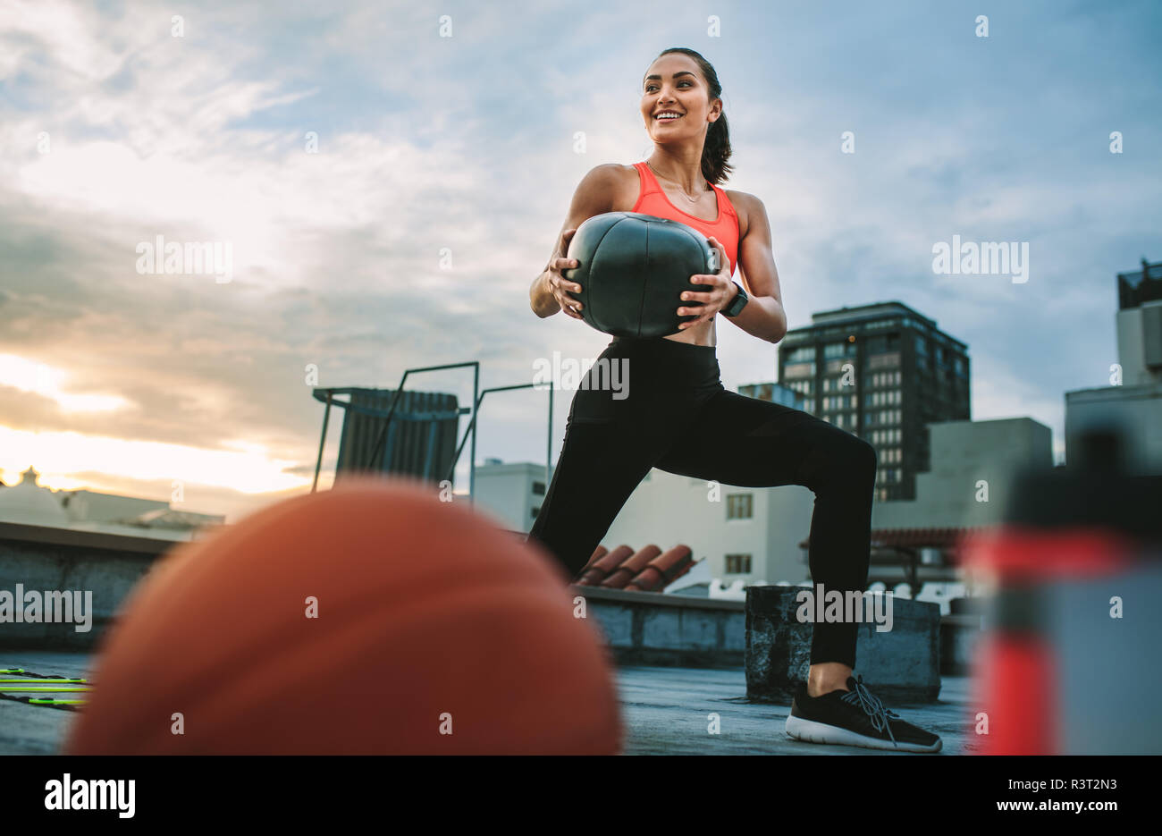 Weibliche Athletin, die einen Medizinball auf dem Dach hält. Fitnesstraining-Frau mit Medizinball mit Basketball und Wasser bo Stockfoto