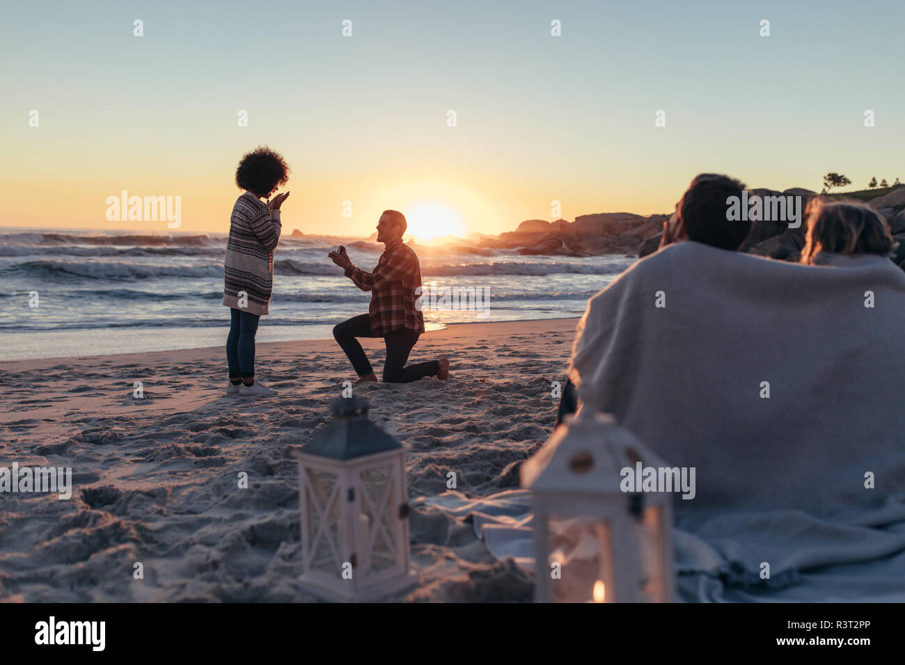 Mann Schlagt Frau Am Meer Begeistert Heiratsantrag Bei Sonnenuntergang Strand Mit Freunden Sitzen Vor In Eine Decke Gewickelt Stockfotografie Alamy