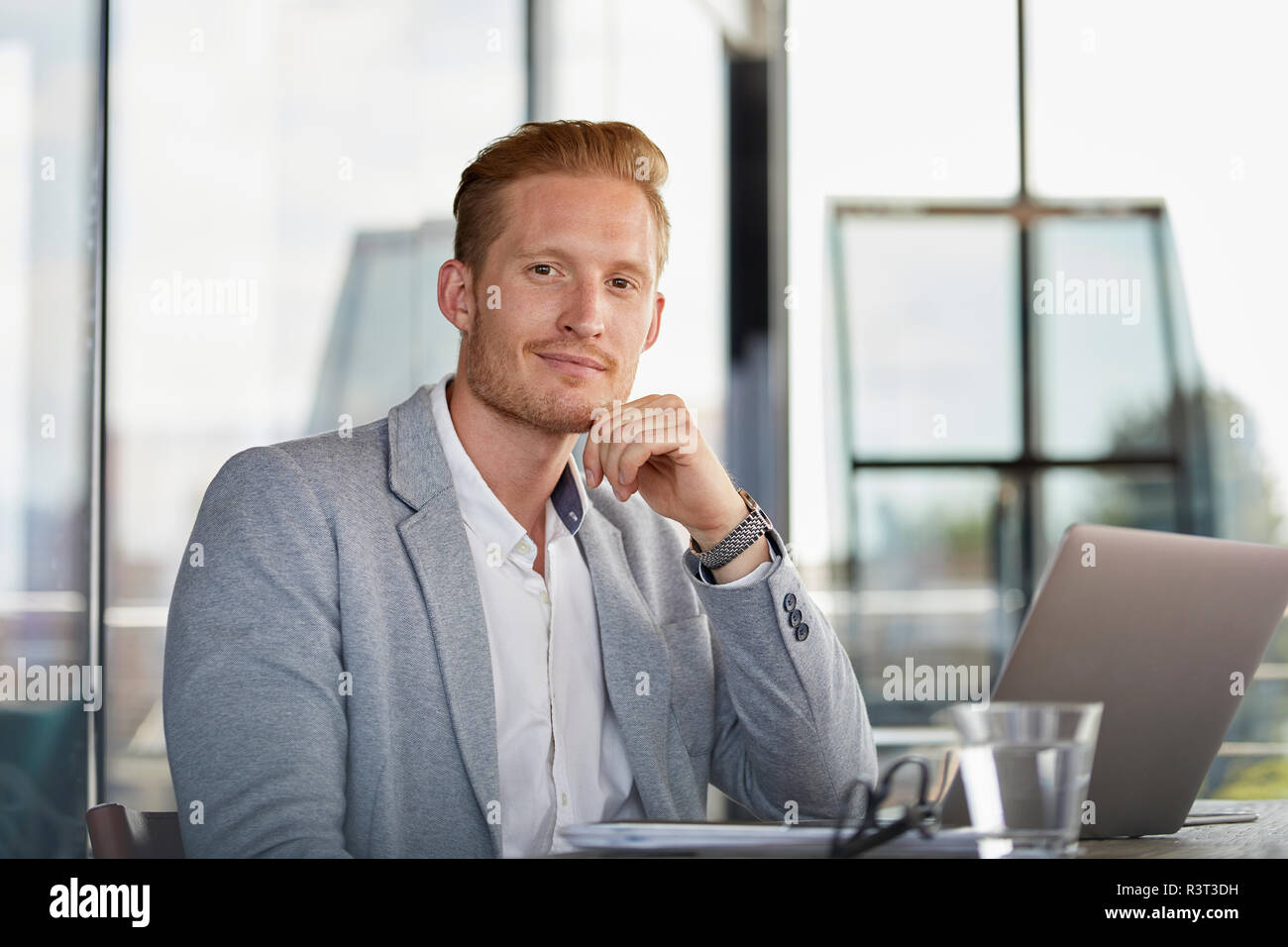 Portrait von zuversichtlich Geschäftsmann mit Laptop auf dem Schreibtisch im Büro Stockfoto