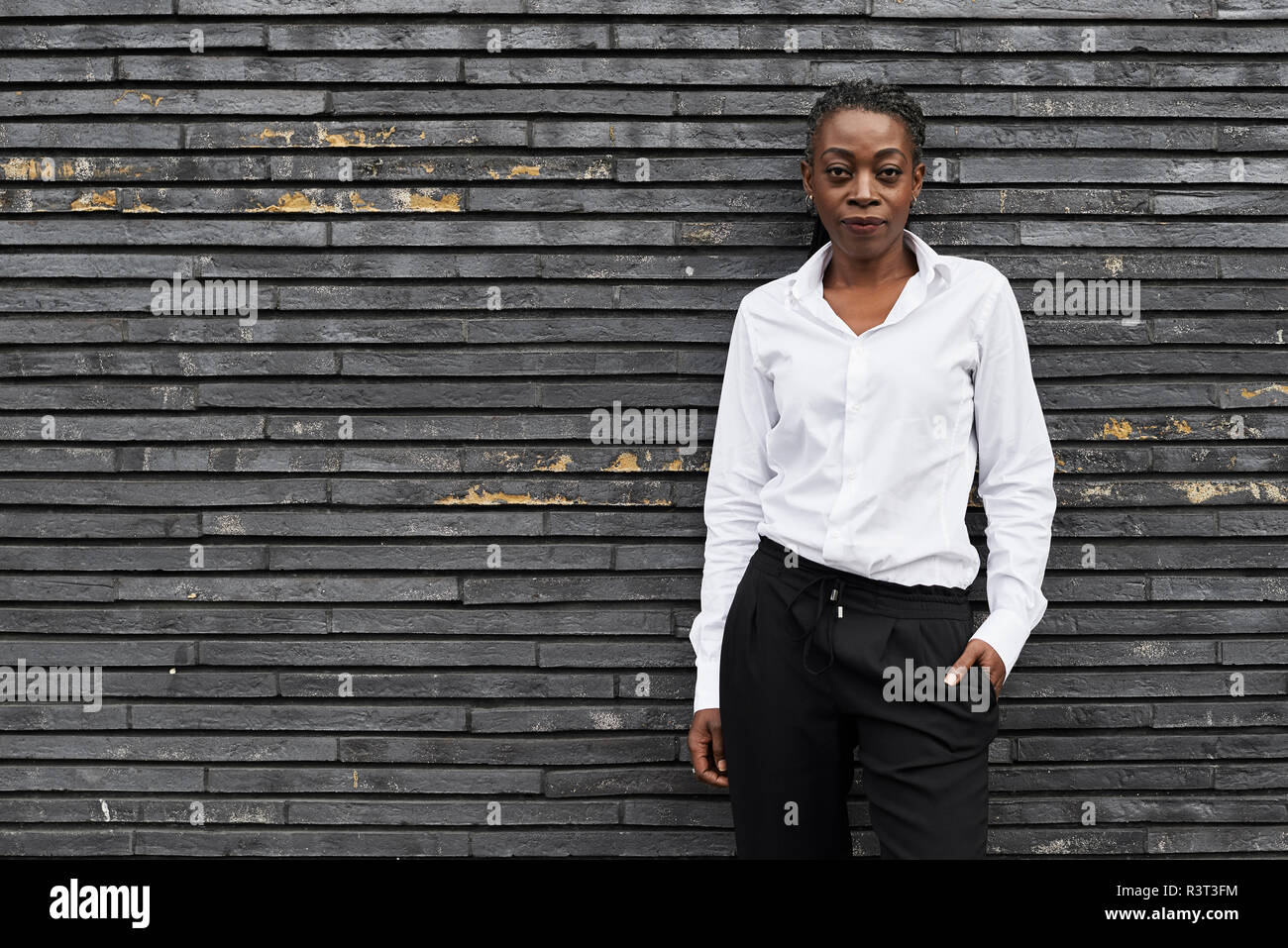 Portrait von smart Geschäftsfrau, tragen weiße Hemd und schwarzen Hosen gegen die Wand lehnt Stockfoto