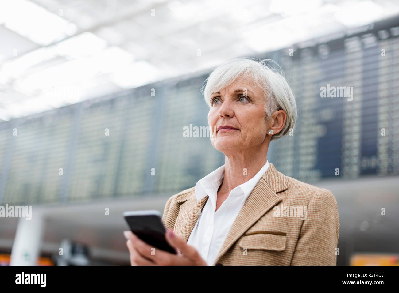 Senior Geschäftsfrau holding Handy am Flughafen Stockfoto