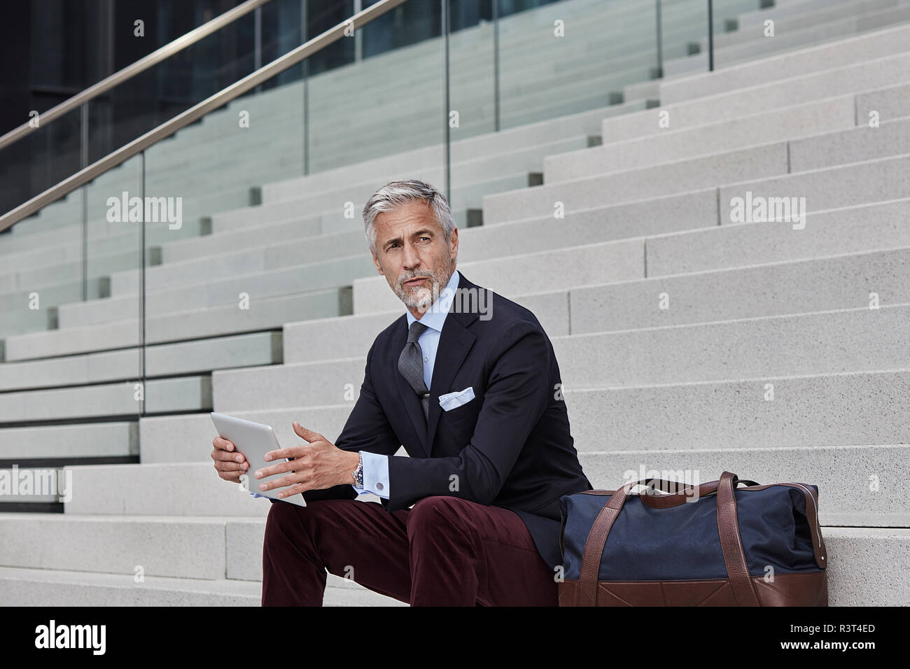 Portrait von modischen Geschäftsmann mit Reisetasche und Tablet sitzen auf Treppen Stockfoto