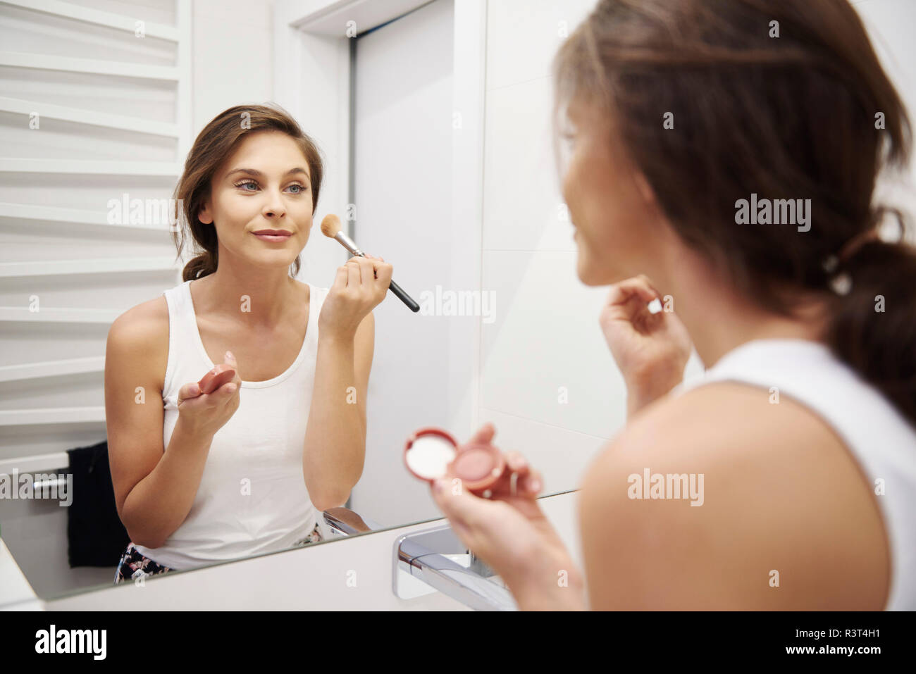 Spiegelbild der lächelnden jungen Frau Anwendung Make-up im Badezimmer Stockfoto