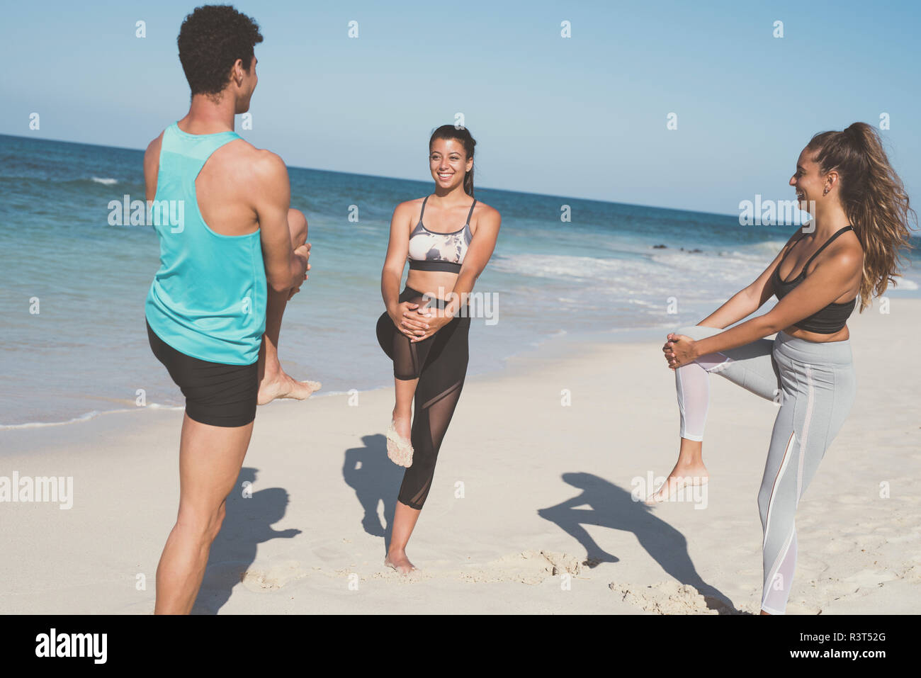 Spanien, Kanarische Inseln, Fuerteventura, zwei junge Frauen und ein junger Mann stretching am Strand Stockfoto