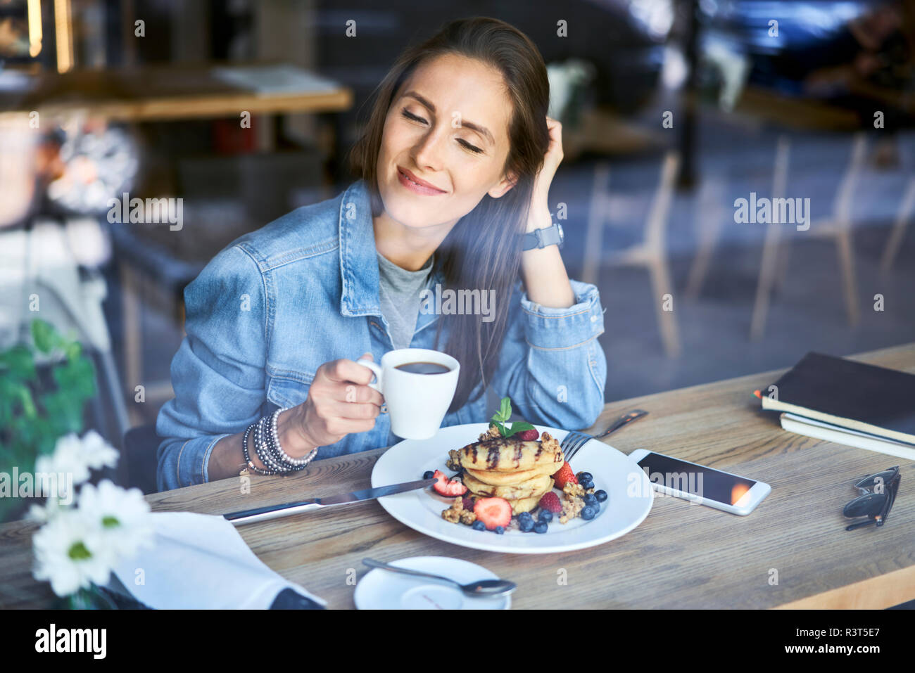 Lächelnde junge Frau mit Pfannkuchen und Kaffee im Cafe Stockfoto