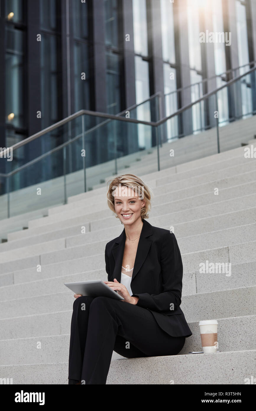 Portrait von lächelnden Geschäftsfrau mit Tablet und Kaffee zu sitzen auf der Treppe vor der modernen Bürogebäude gehen Stockfoto