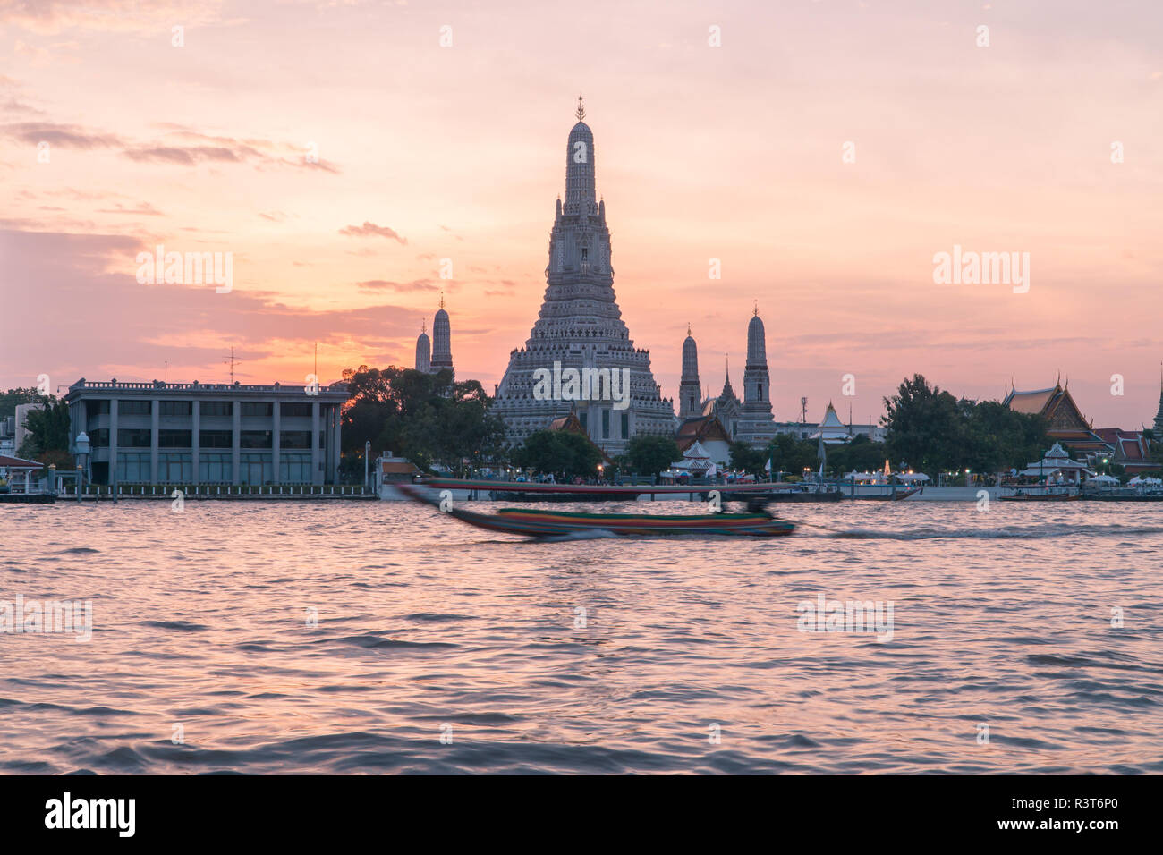 Beliebtes Touristenziel Wat Arun Tempel der Morgendämmerung über den Chao Phraya Fluss in Bangkok, Thailand bei Sonnenuntergang mit traditionellen langen Schwänzbooten Stockfoto