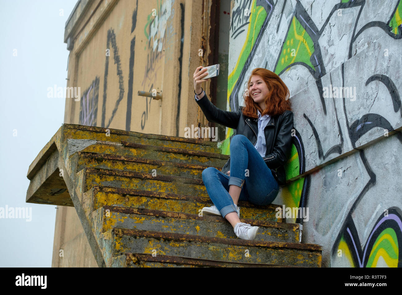 Italien, Finale Ligure, rothaarige Mädchen im Teenageralter ltaking selfie vor Graffiti an der Wand Stockfoto
