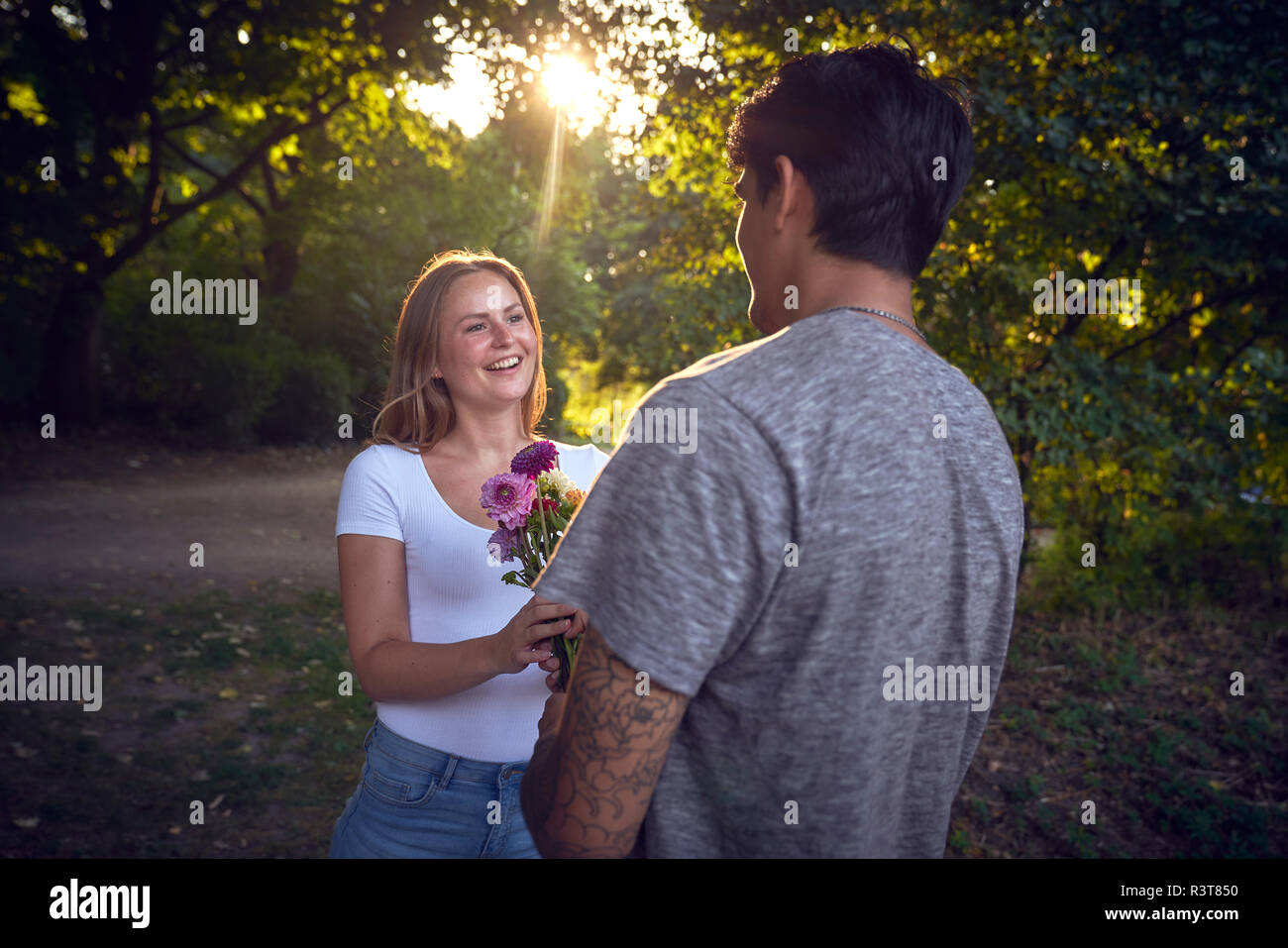 Junger Mann, seine Freundin in einem Park, ihre Geschenke mit Blumen Stockfoto