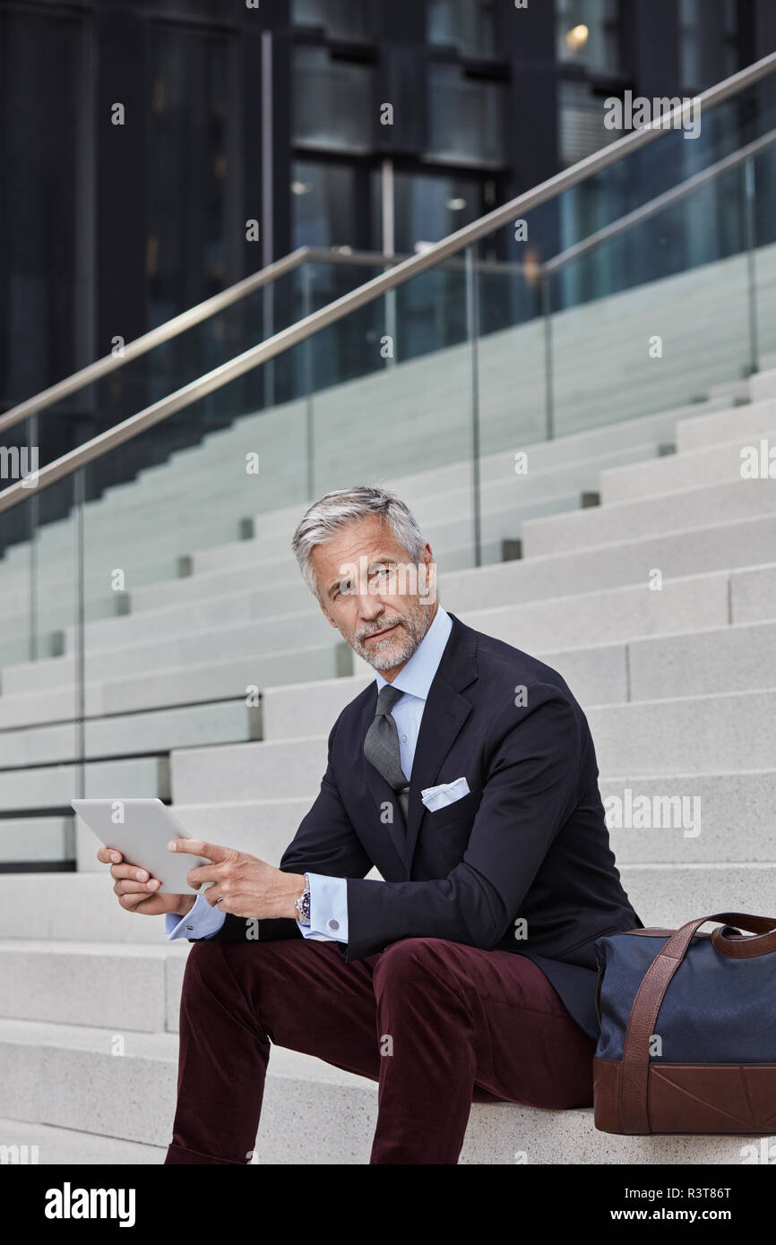Portrait von modischen Geschäftsmann mit Reisetasche und Tablet sitzen auf Treppen Stockfoto