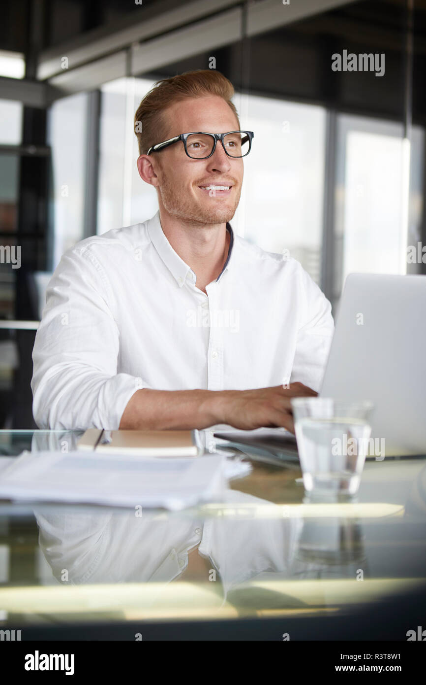 Lächelnd Geschäftsmann mit Laptop auf dem Schreibtisch im Büro Stockfoto