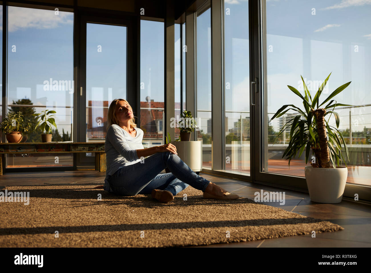 Entspannt reife Frau sitzt auf dem Teppich im Sonnenlicht zu Hause Stockfoto
