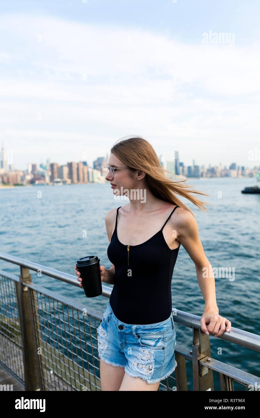 Junge Frau über den East River suchen, holding Tasse Kaffee Stockfoto