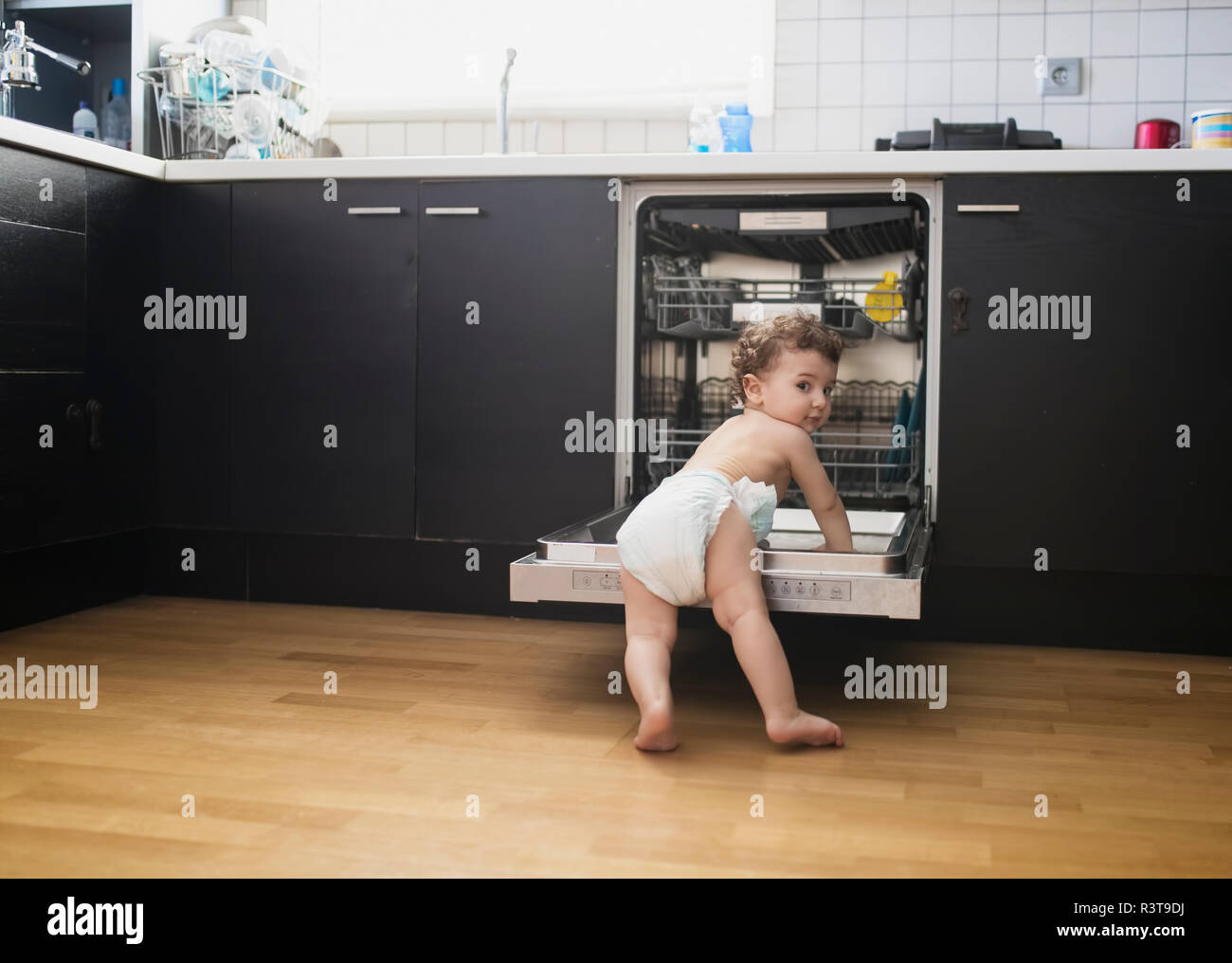Portrait von baby boy tragen Windel Erkundung Geschirrspüler in der Küche Stockfoto