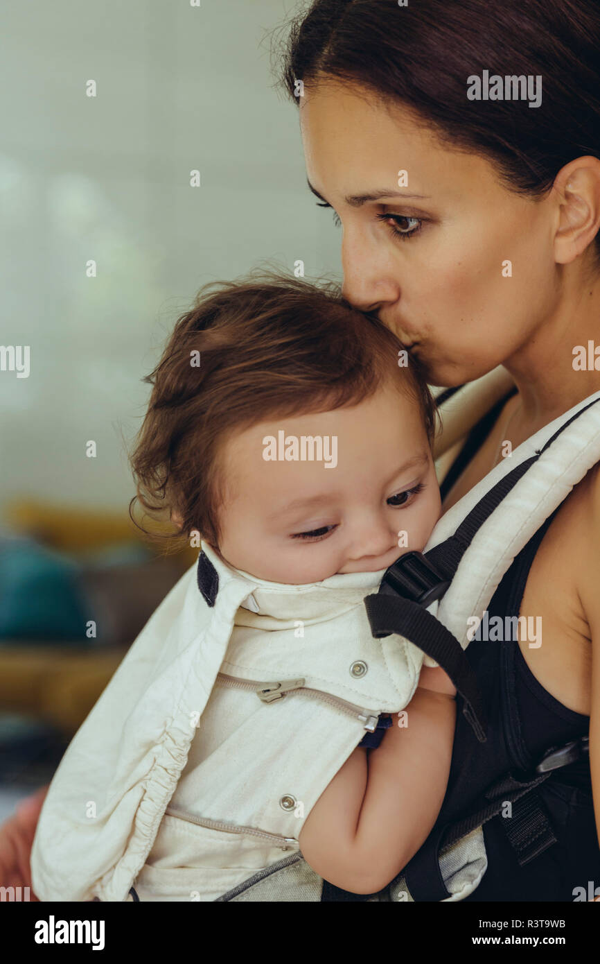 Mutter küssen und ihr Baby Mädchen tragen in der Schlinge zu Hause Stockfoto