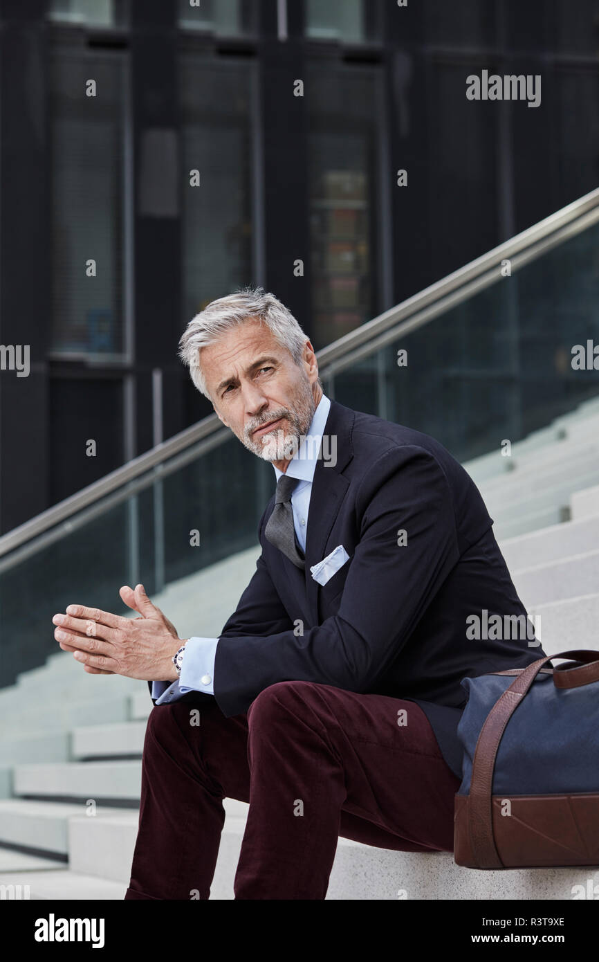 Portrait von modischen Geschäftsmann mit Reisetasche sitzen auf der Treppe im Freien Stockfoto