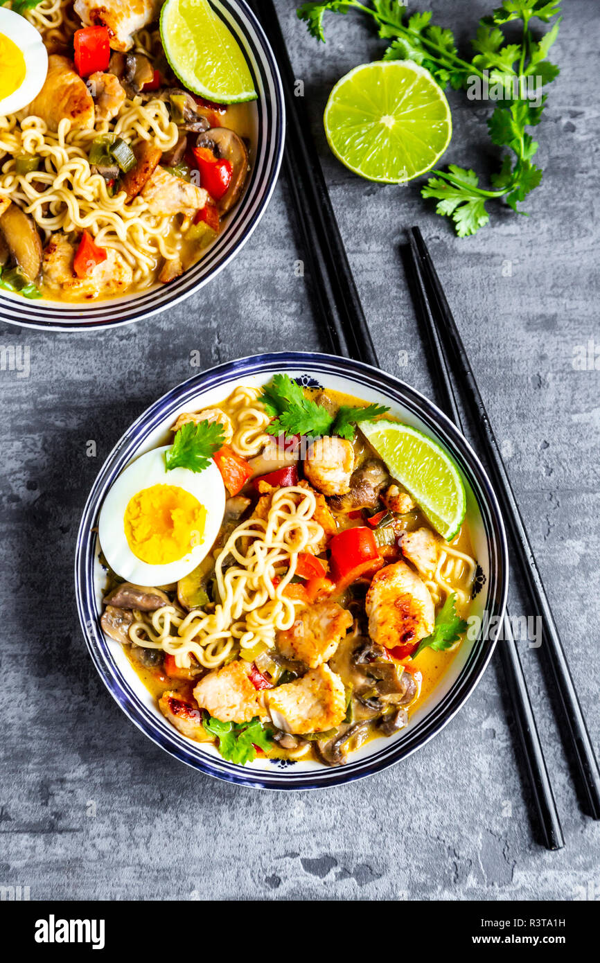 Ramen Suppe mit Ei, Nudeln, Hähnchen Fleisch, Paprika, Pilze, Frühlingszwiebeln, Limette und Koriander Stockfoto