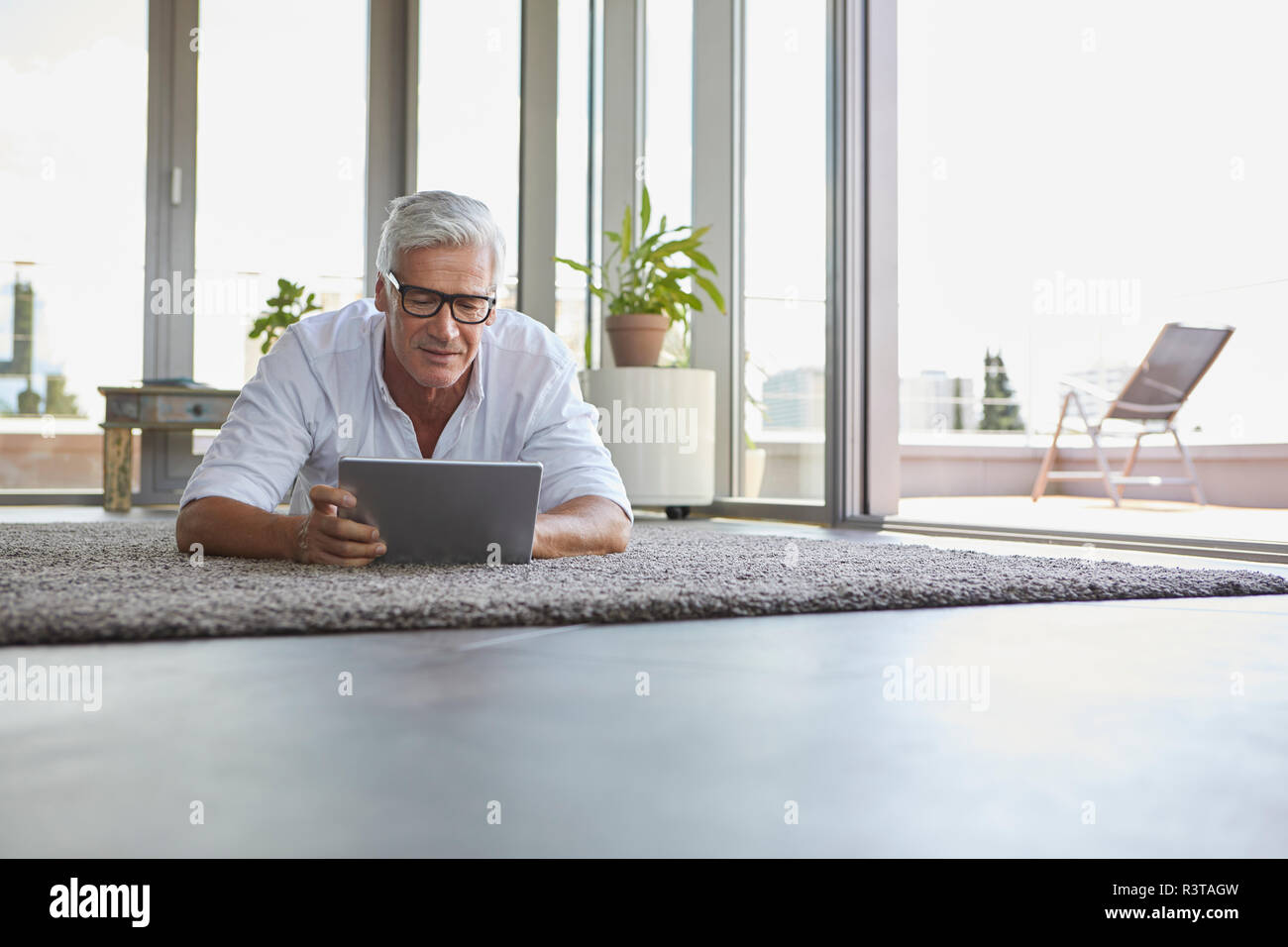 Reifer Mann liegen auf dem Teppich zu Hause mit der Tablette Stockfoto