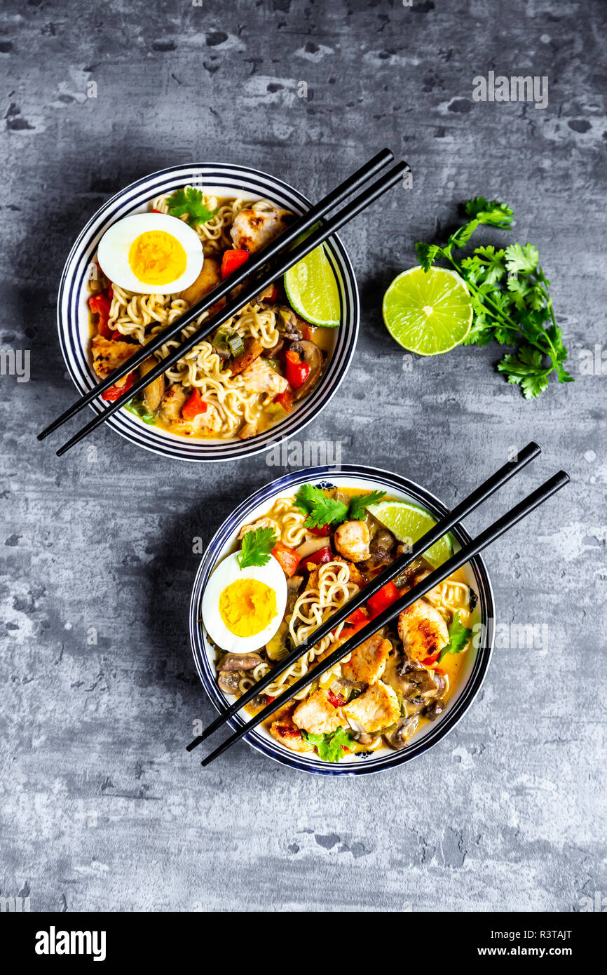 Ramen Suppe mit Ei, Nudeln, Hähnchen Fleisch, Paprika, Pilze, Frühlingszwiebeln, Limette und Koriander Stockfoto