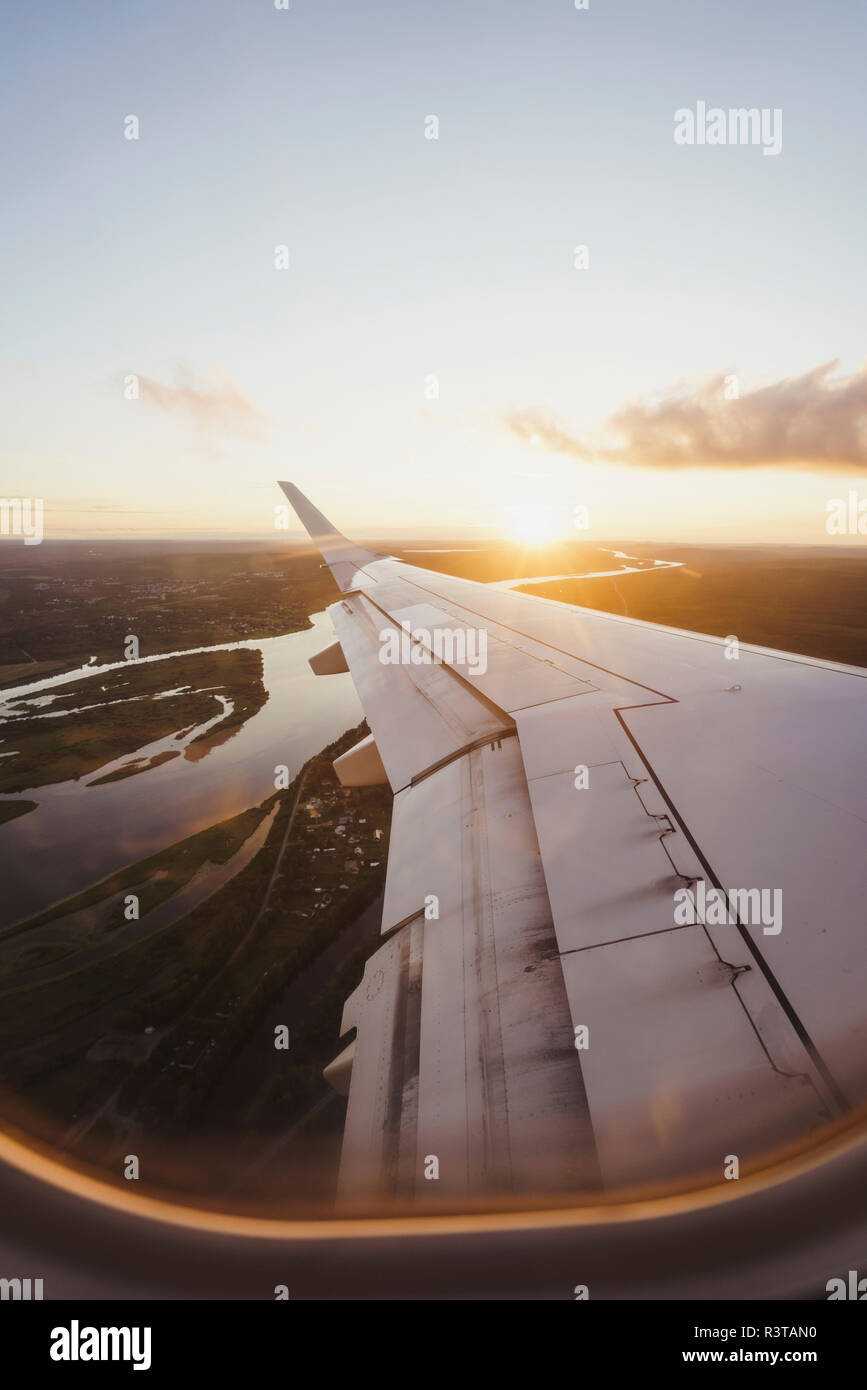 Blick aus dem Fenster auf die Flügel eines Flugzeugs bei Sonnenuntergang Stockfoto