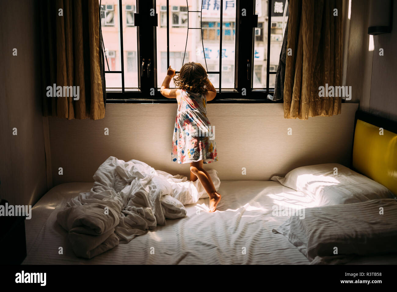 China, Hongkong, Mong Kok, zurück Blick auf kleine Mädchen stehen, barfuß auf dem Bett Blick aus Fenster Stockfoto